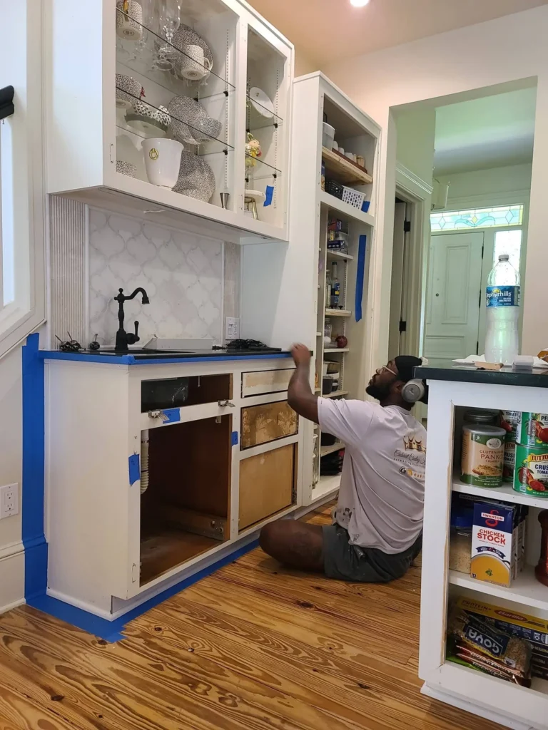 Expert painter refinishing kitchen island or wet bar cabinets Professional painter refinishing lower white kitchen island cabinets with blue tape protection.